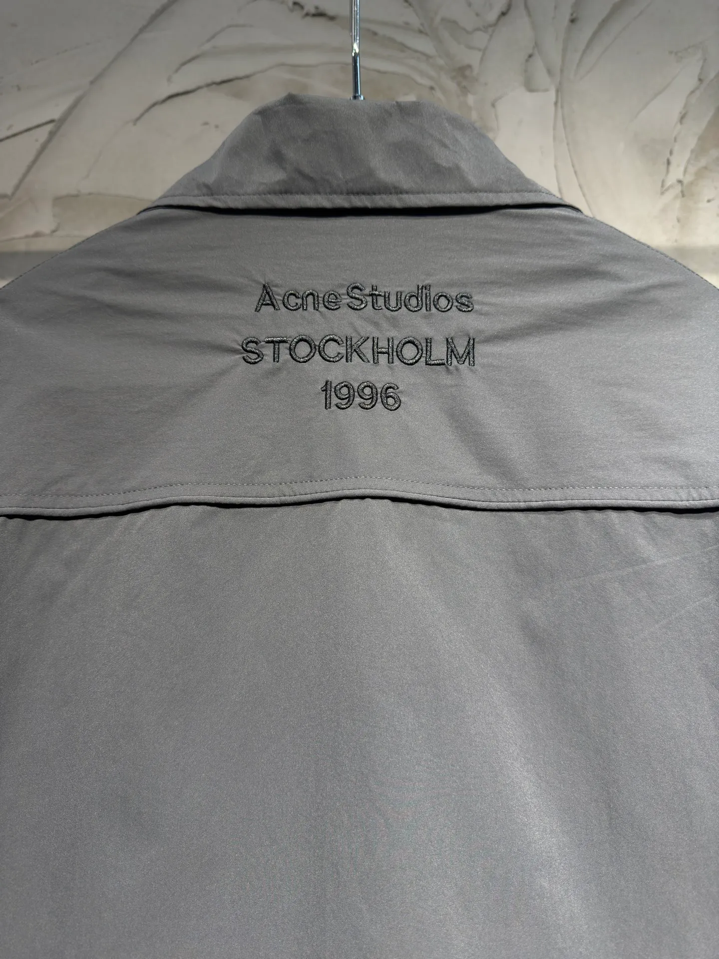 Acne Studios 26SS Large Lapel Short Jacket The fabric is made of 100% nylon (nylon/polyamide fiber) 75D high-density wrinkled nylon. The fabric has been permanently pressed and shaped by high temperature, and washed with high-pressure wrinkles at the factory to form its own irregular texture, permanently retaining the wrinkled texture, which will not disappear after washing. Matte matte coating removes the plastic glossy surface of nylon itself to create a low-key matte paper feel. Three-proof micro-coating, weak waterproof, anti-fouling, anti-static treatment, not easy to get dust. The interior is made of full-width mesh Breathable nylon lining, which reduces the stickiness of the nylon fabric to the body, improves air circulation, prevents sweating from sticking to the skin, and the zipper does not rub against the skin. The version adopts the raglan split topstitching process, and the front and rear panels are divided diagonally to expose even stitching. The three-dimensional dropped shoulders are loose and the fit is increased to increase the margin of movement. The back neckline is three-dimensional and high-density computer embroidered, and the embroidery lines are dense and not prickly. Customized all-metal matte nylon zipper, Genuine Leather embossed brand letters on the zipper leather tab, zipper tape with same color nylon fit to the body, double-locked reinforcement on both sides of the zipper to prevent pulling and tearing. Color: Gray Size: S M L